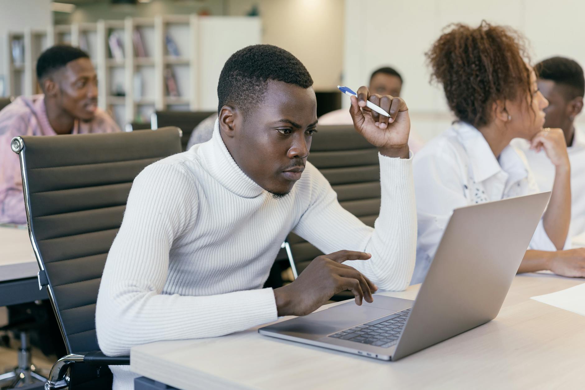 Young man intently working on a laptop in an office setting, concentrating on his task.