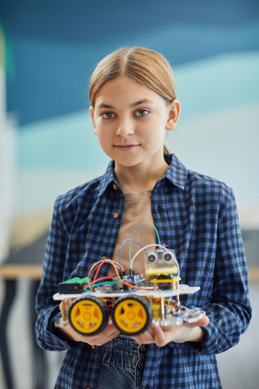 A young girl in a checkered shirt holds a DIY robotic project, showcasing technology and creativity.