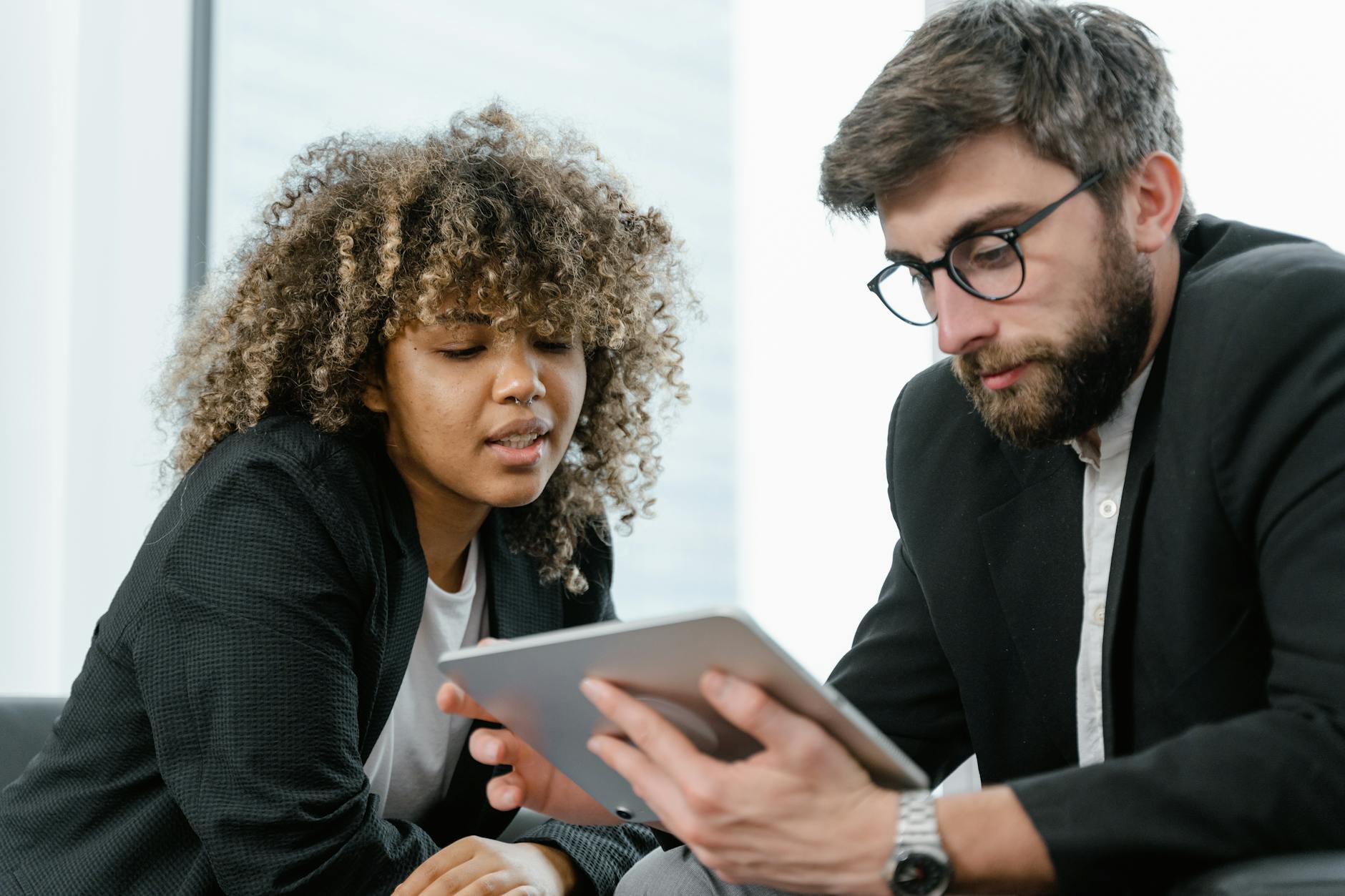 Two business professionals reviewing data on a tablet, fostering collaboration and teamwork in a modern office setting.