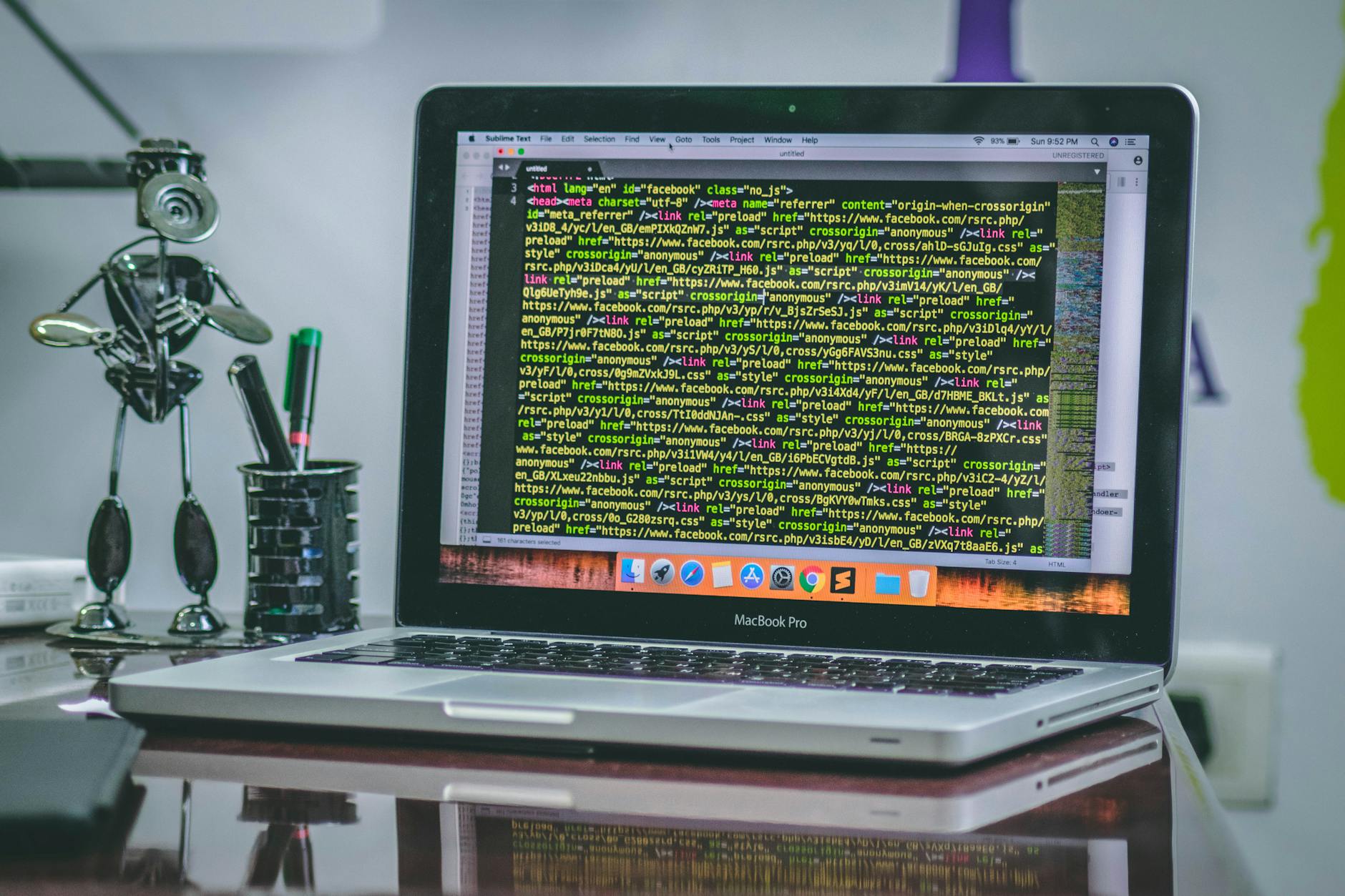 A sleek MacBook Pro displaying code on a desk with office tools and creative decorations.