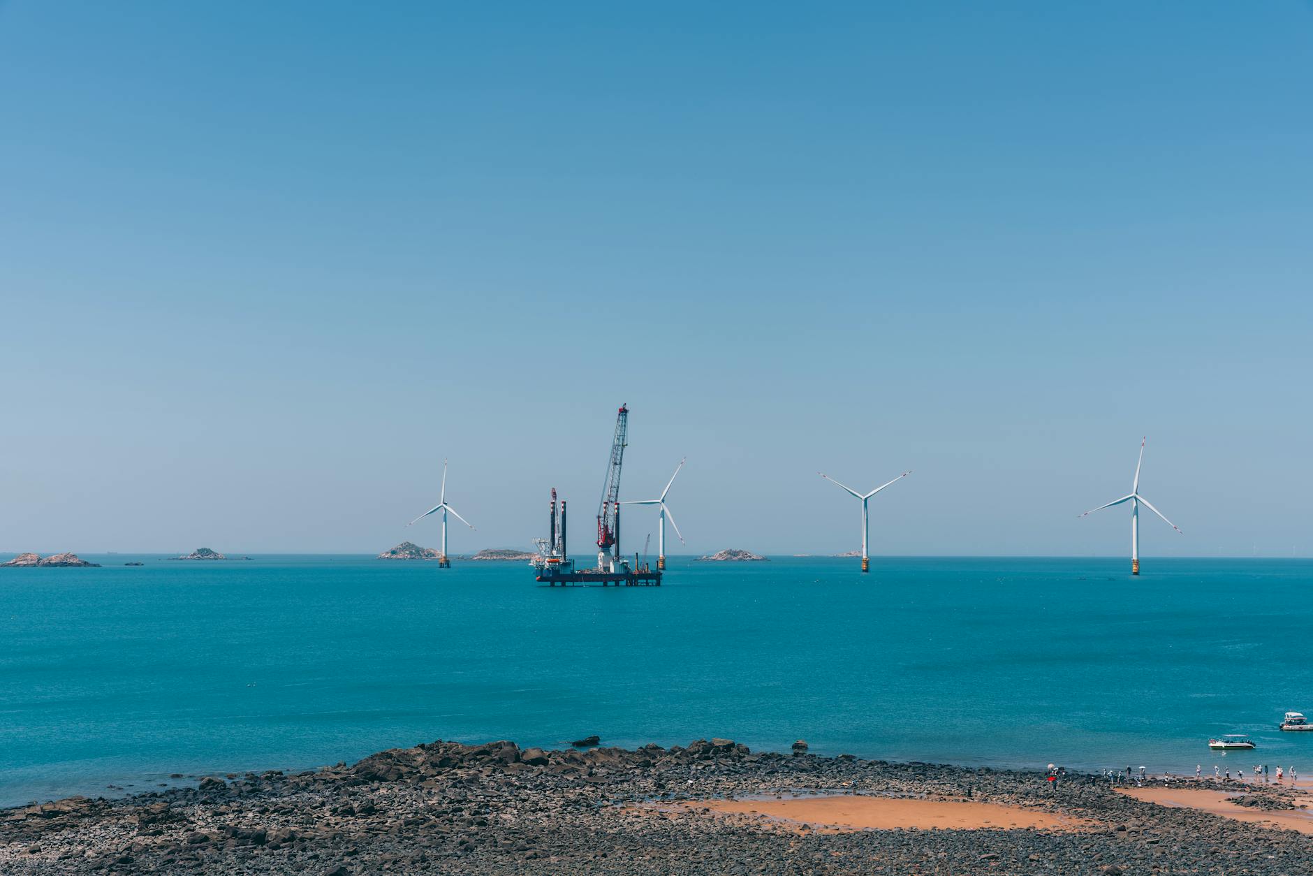 A serene view of offshore wind turbines against a clear blue sky with calm ocean waters.