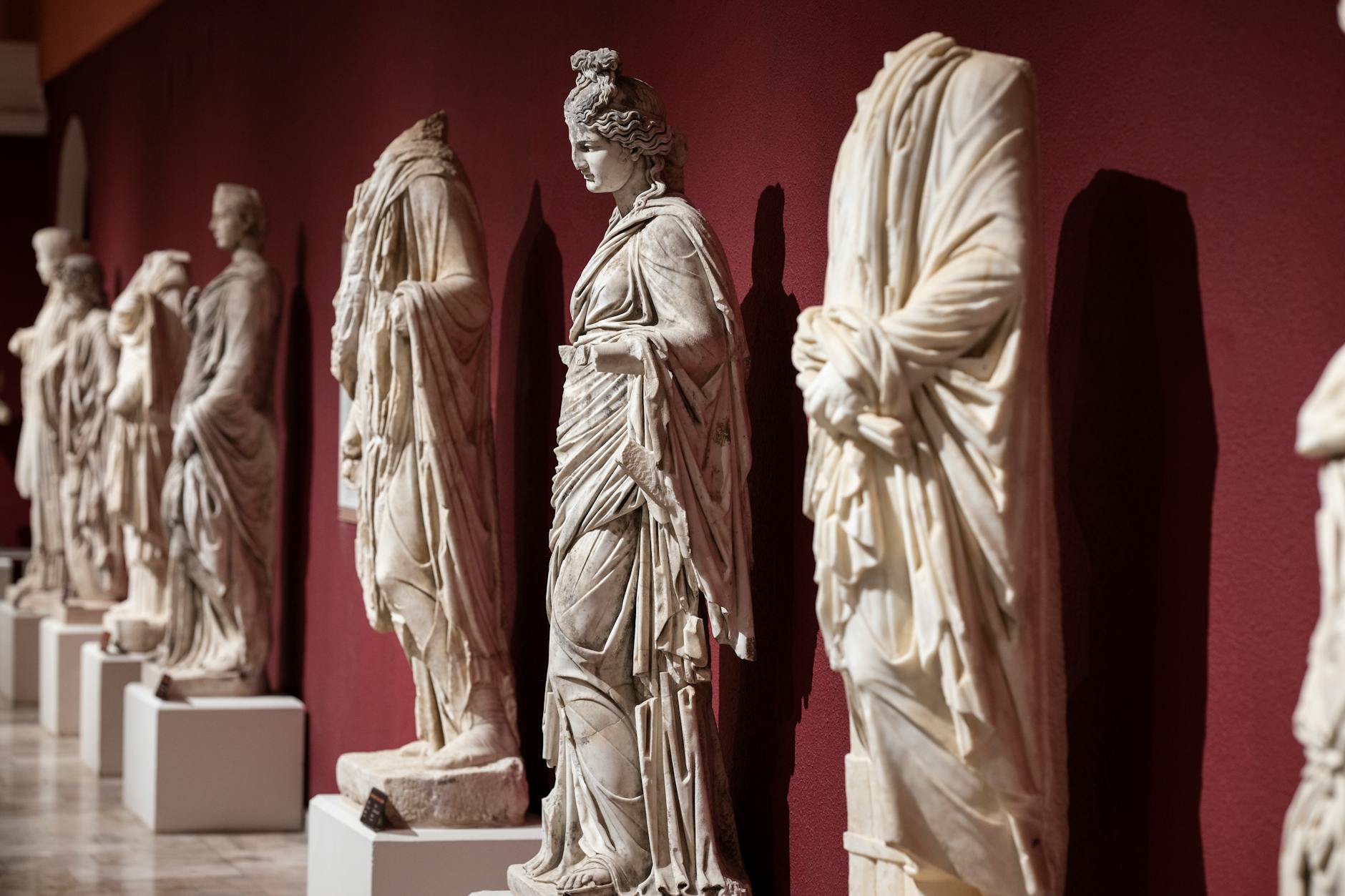 Collection of ancient Roman statues on display in a museum with a red wall backdrop.