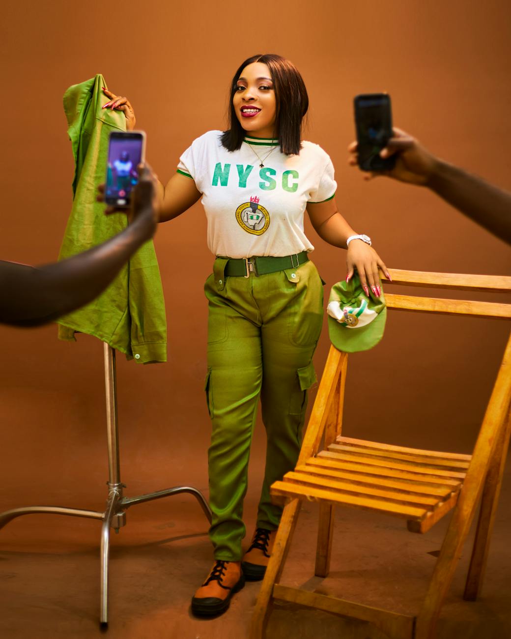 Woman poses in NYSC uniform surrounded by mobile cameras.