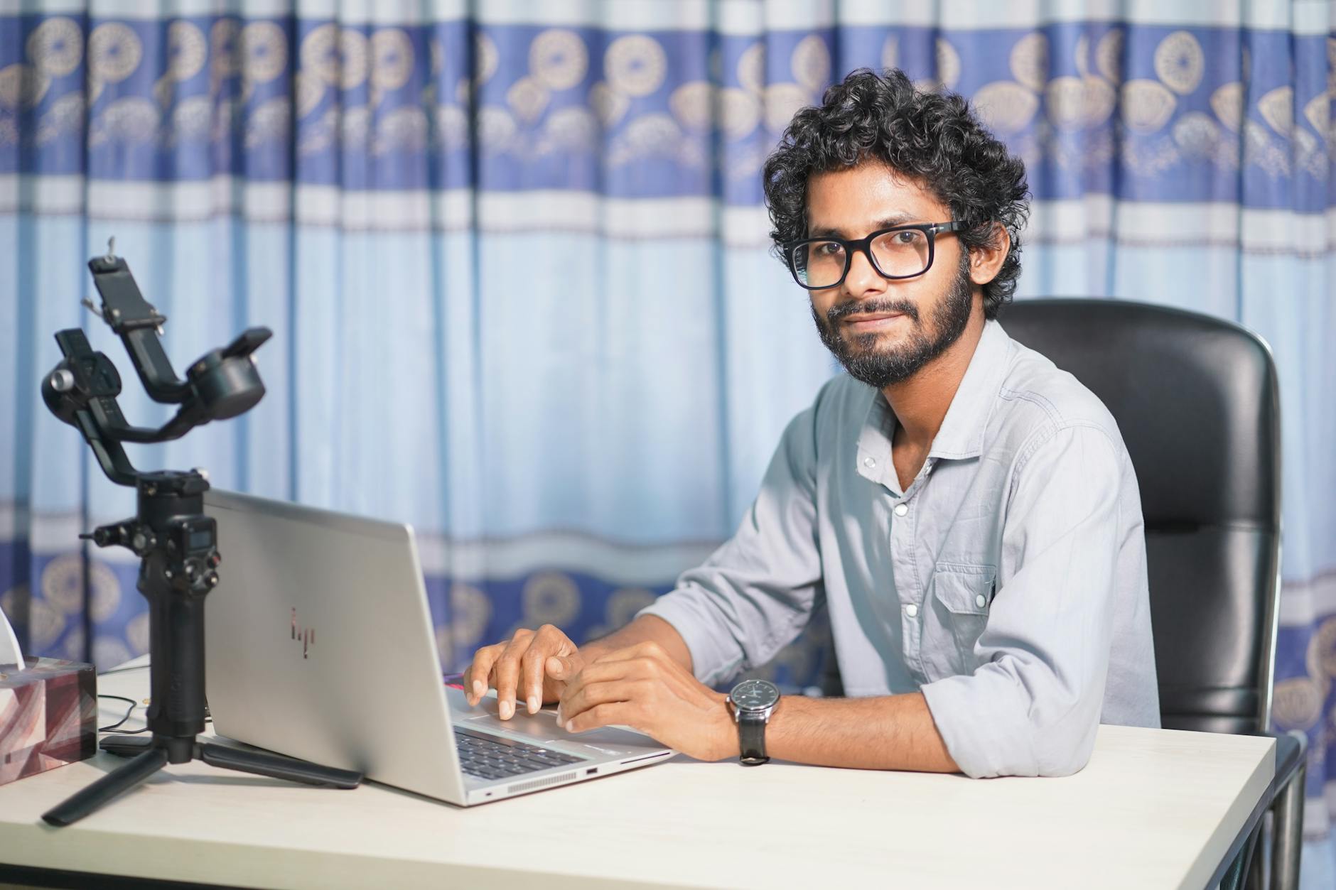 Portrait of a web developer with a laptop and camera, working at his office desk in a modern setup.