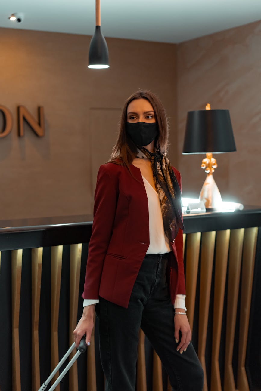 A fashionable hotel receptionist wearing a mask assists guests at the front desk.