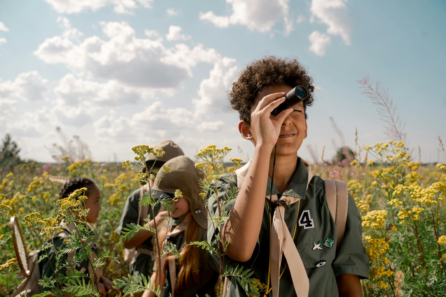 Group of young scouts observing nature with spotting scope in a summer field.