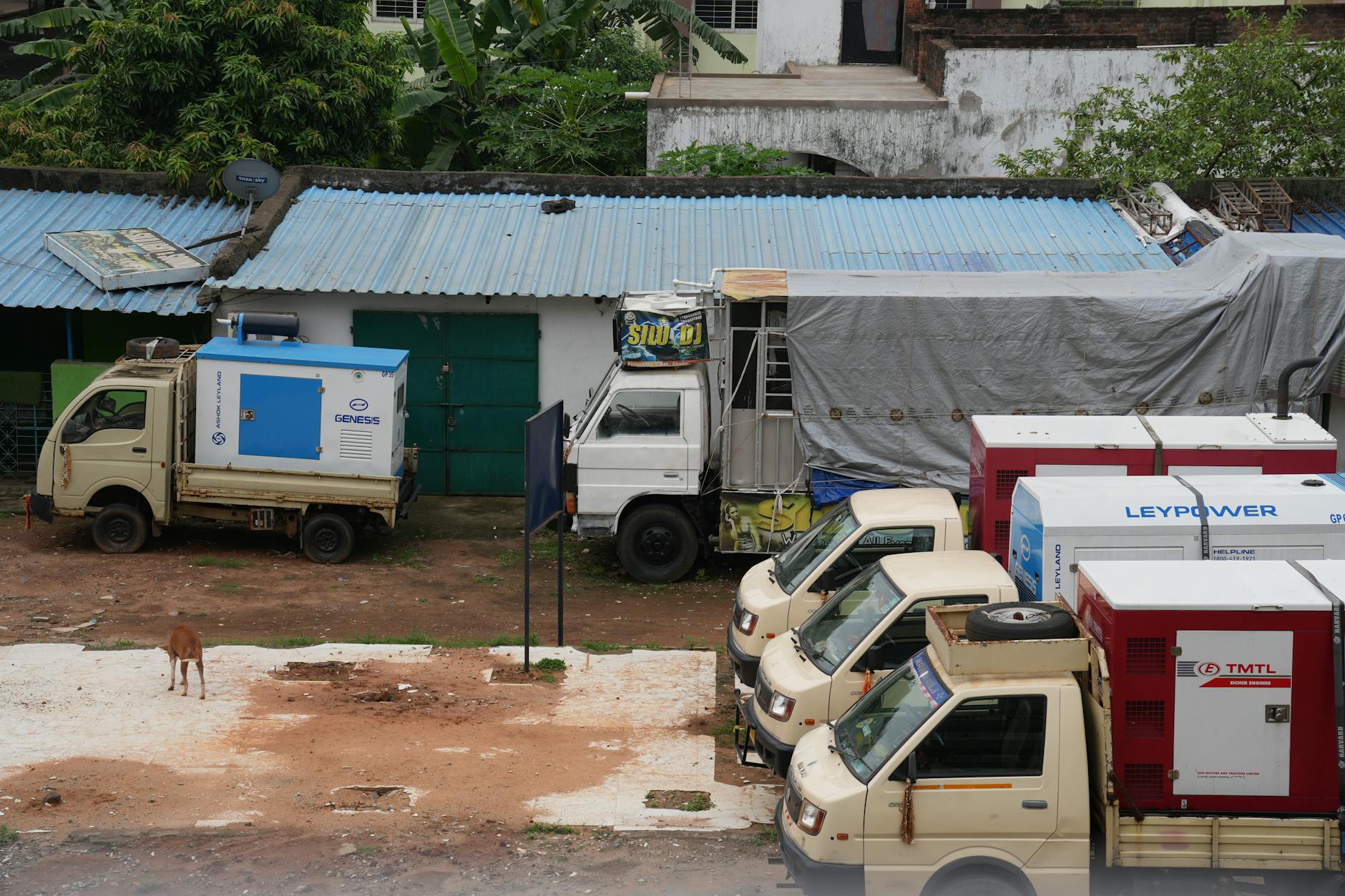 A row of parked utility trucks with generators beside a building outdoors.