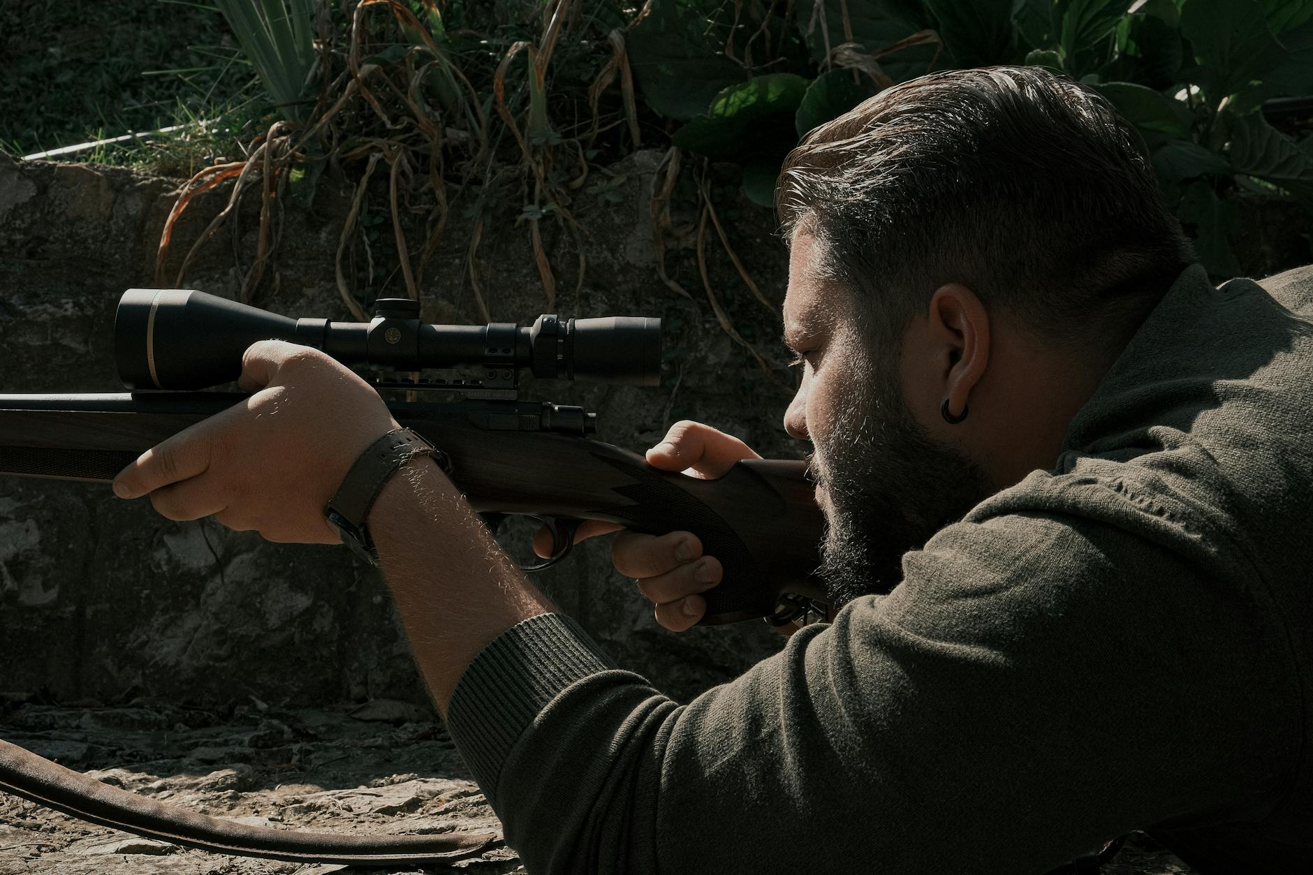 Focused man in outdoor setting aiming rifle with scope for precision shooting.
