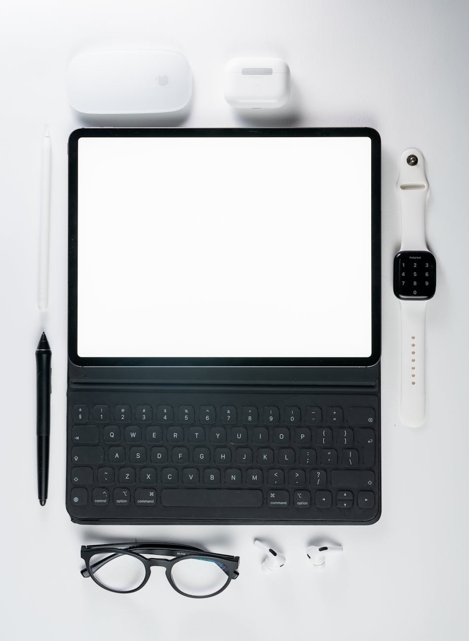 Flat lay of tablet, keyboard, smartwatch, and accessories on a white background.