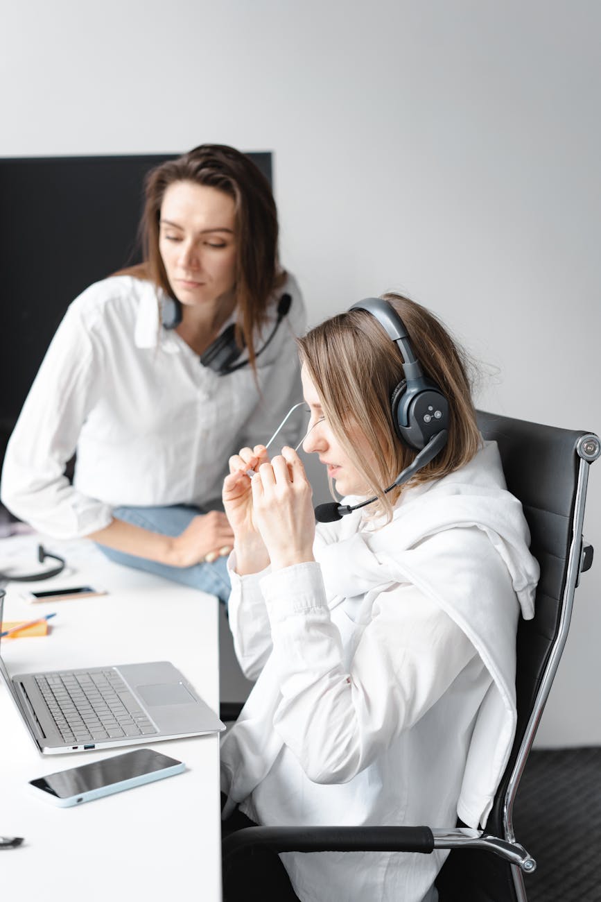 Two female customer service agents discussing work at their desk with headsets.
