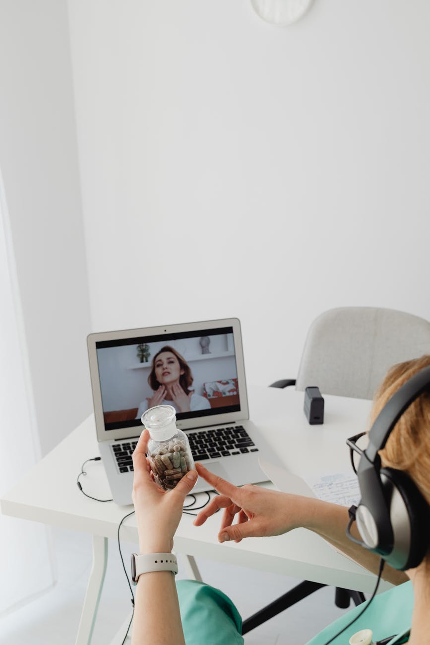 A medical professional in a virtual consultation with a patient, holding a jar while video calling on a laptop.