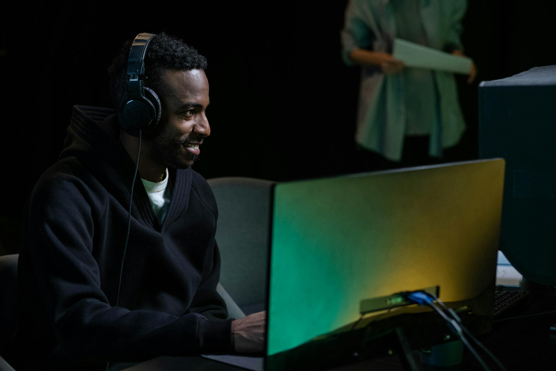 Smiling man in headphones working on audio production in a studio setting, using modern technology.