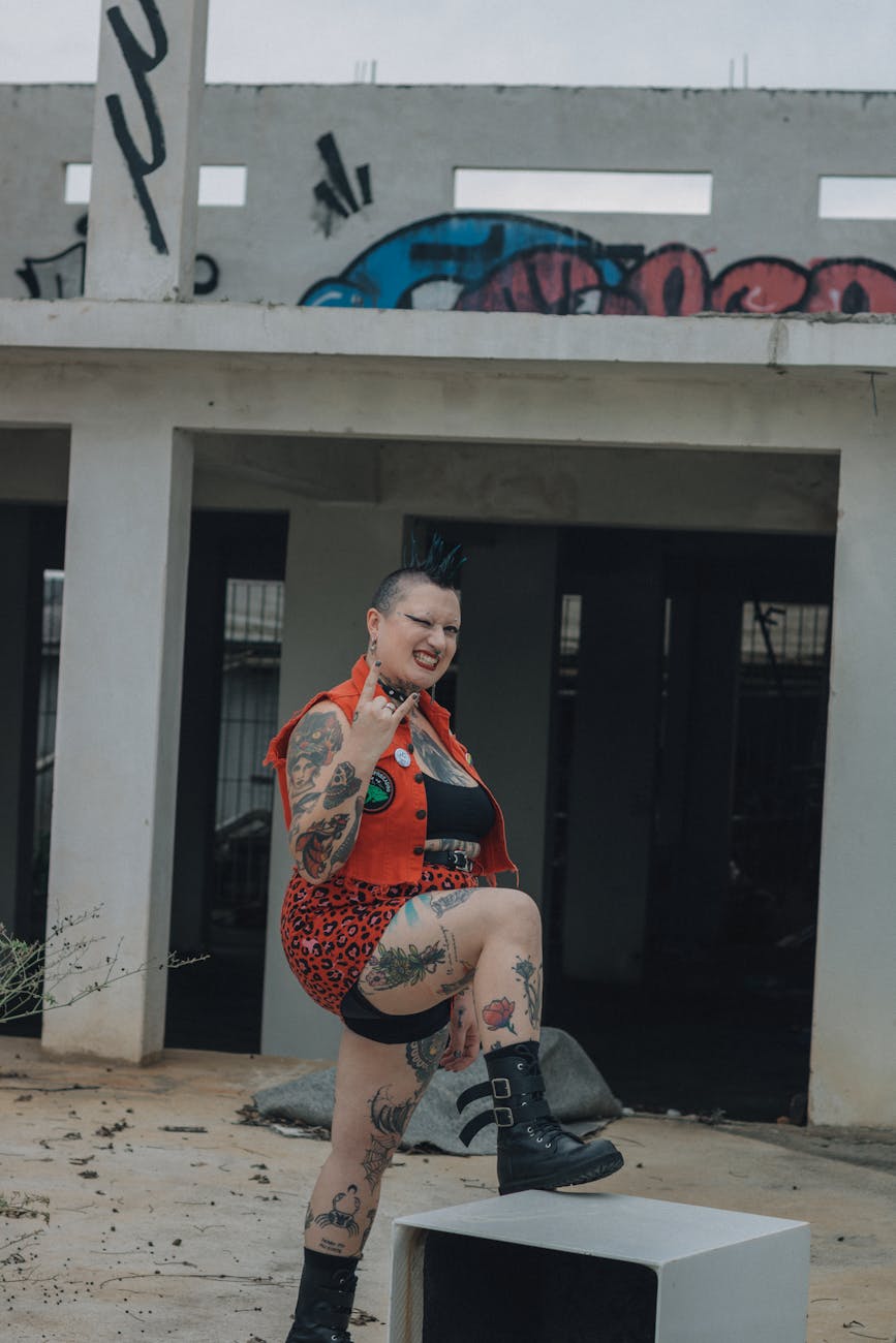 Tattooed woman with punk style poses in an urban environment with graffiti.