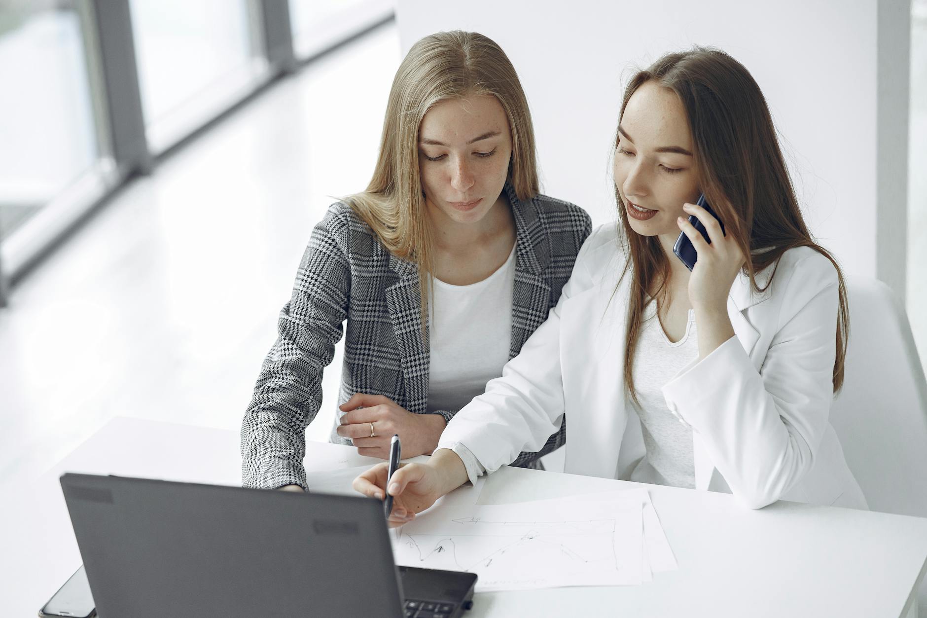 Two businesswomen collaborating at a desk with a laptop and documents.