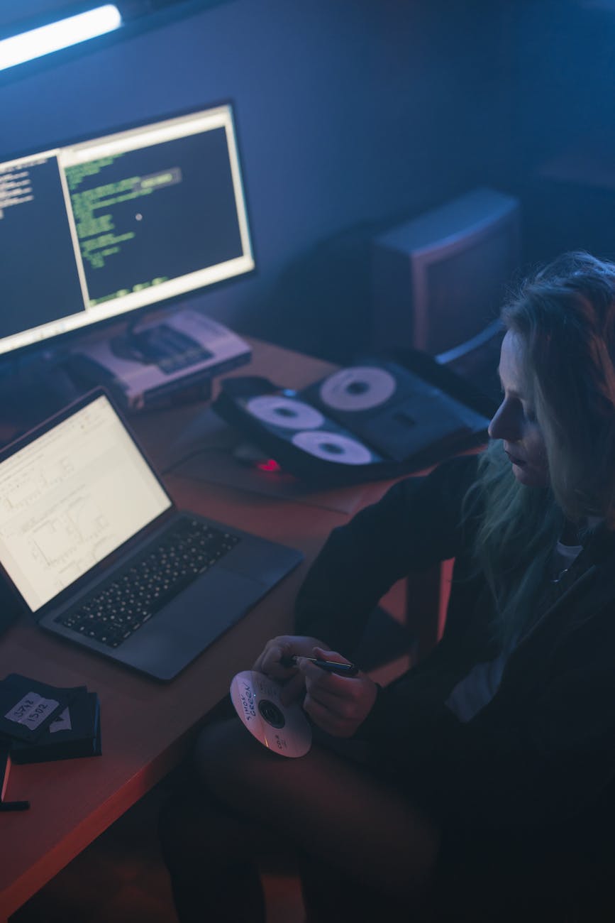 Woman working on a laptop with code on screen, sitting in a dimly lit office holding a CD.