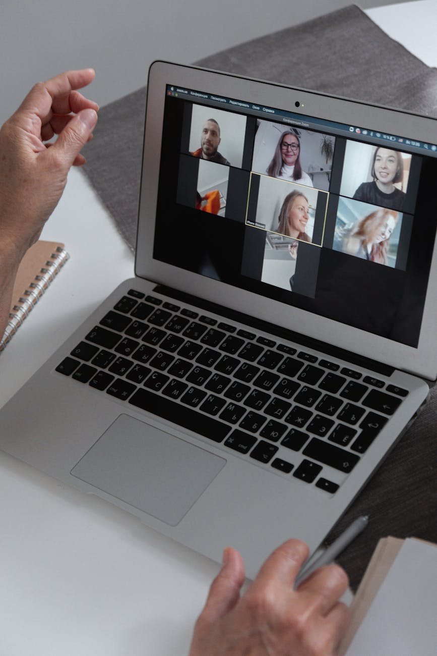 Hands at a laptop showing a group video call in a home office setting.