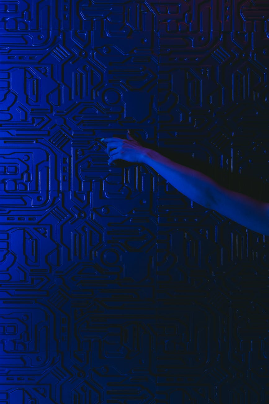 A hand reaches out to touch a futuristic blue circuit patterned wall with dramatic lighting.