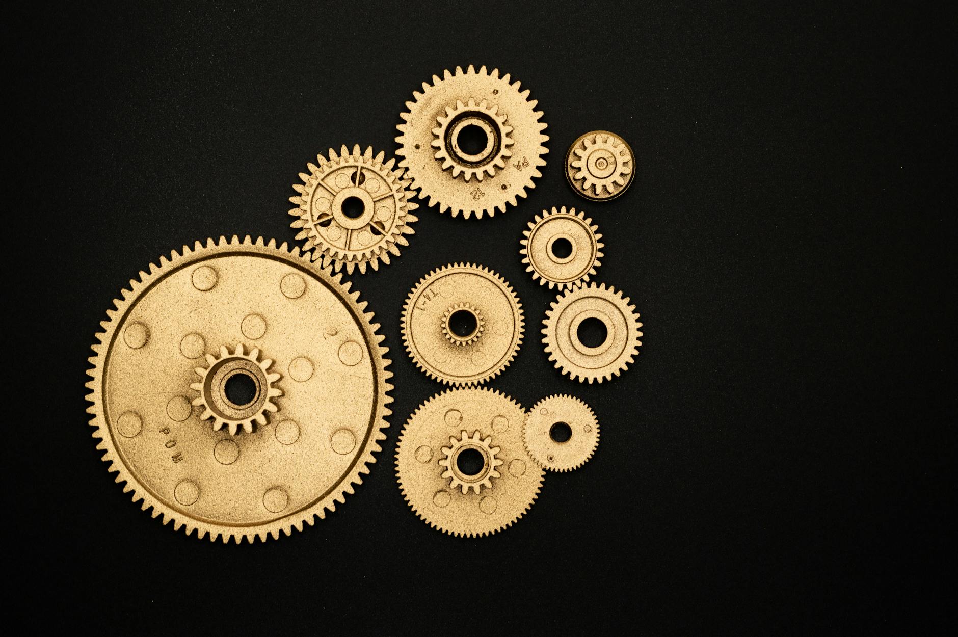 Close-up of golden gears and cogs arranged on a black background, representing teamwork and industry.
