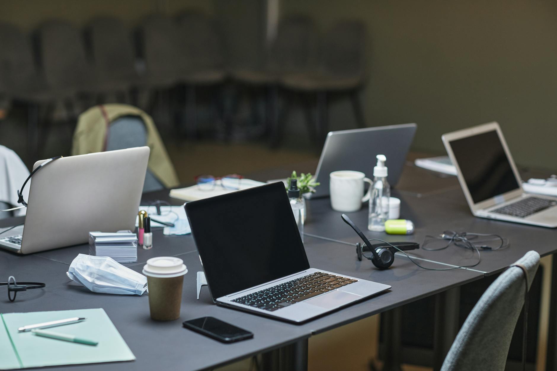 A cluttered office desk setup featuring multiple laptops, coffee cup, and office supplies for a busy workday.