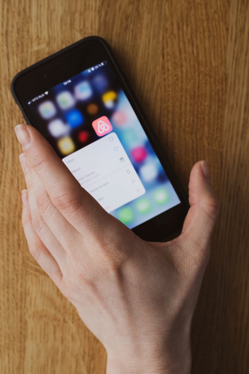 A hand holding a smartphone displaying an app icon on a wooden surface.