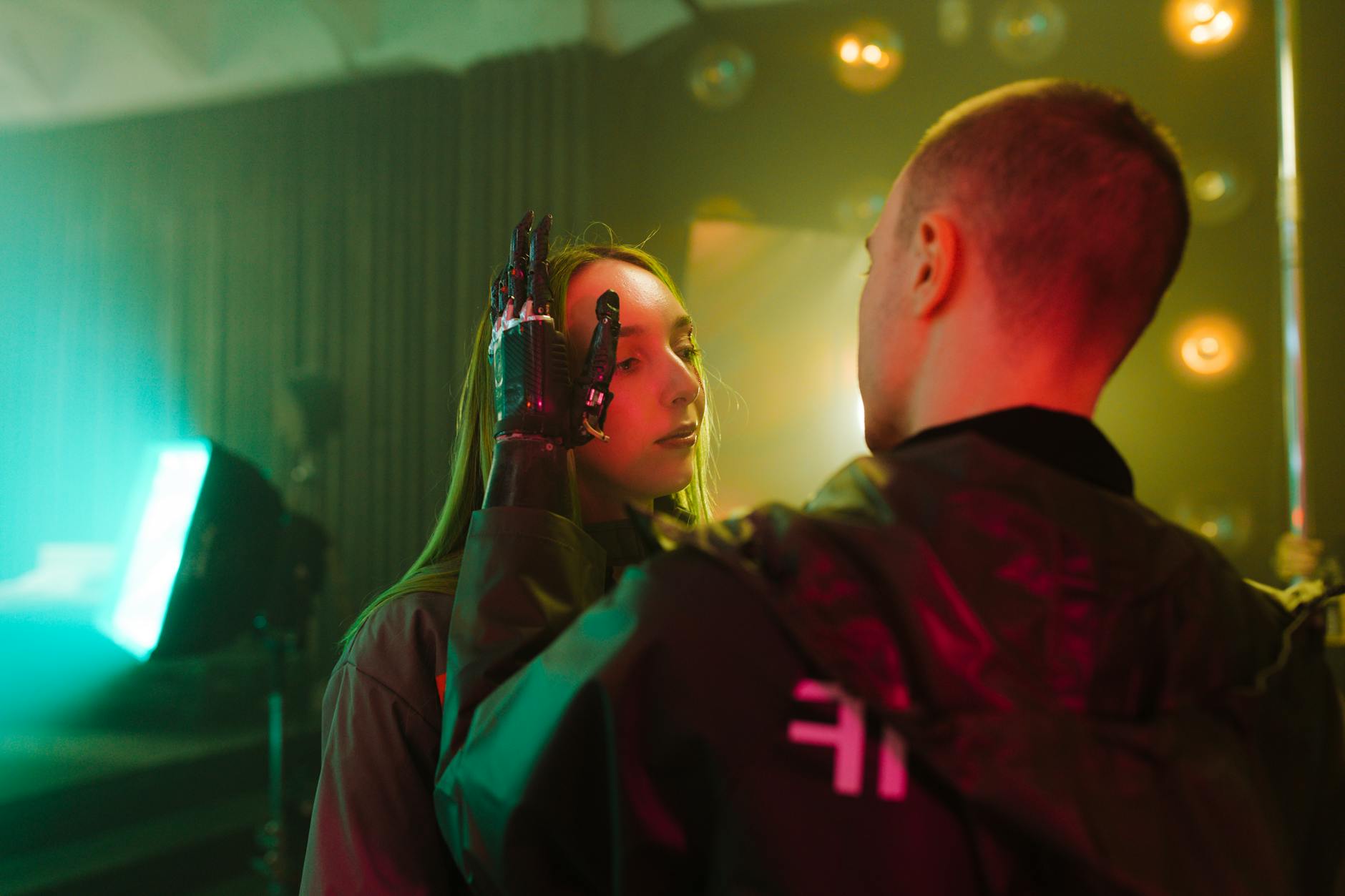 A man with a prosthetic hand gently touches a woman's face in a cyberpunk setting.