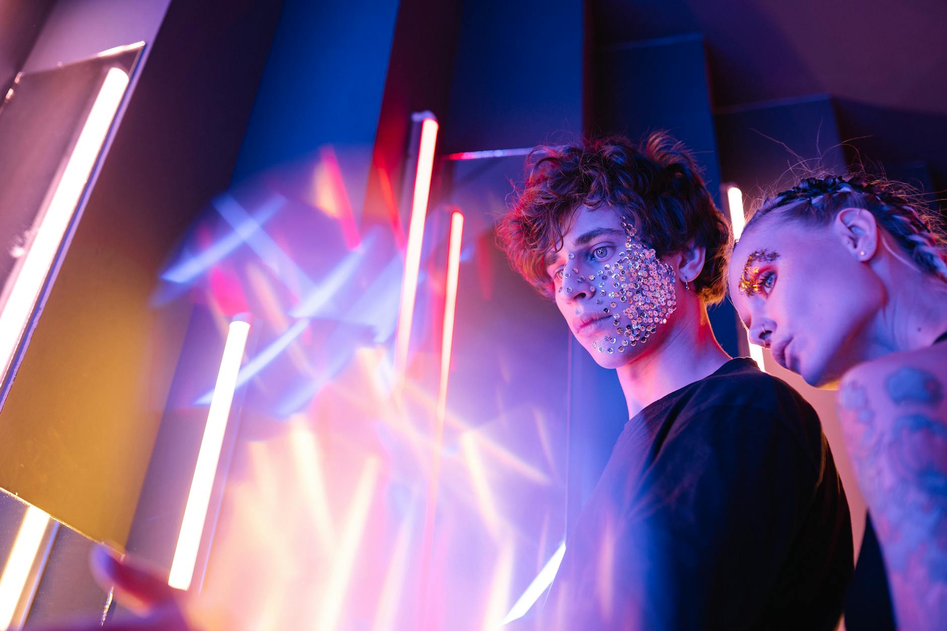 Dynamic studio portrait of two young adults with glitter and neon lights, creating a futuristic vibe.