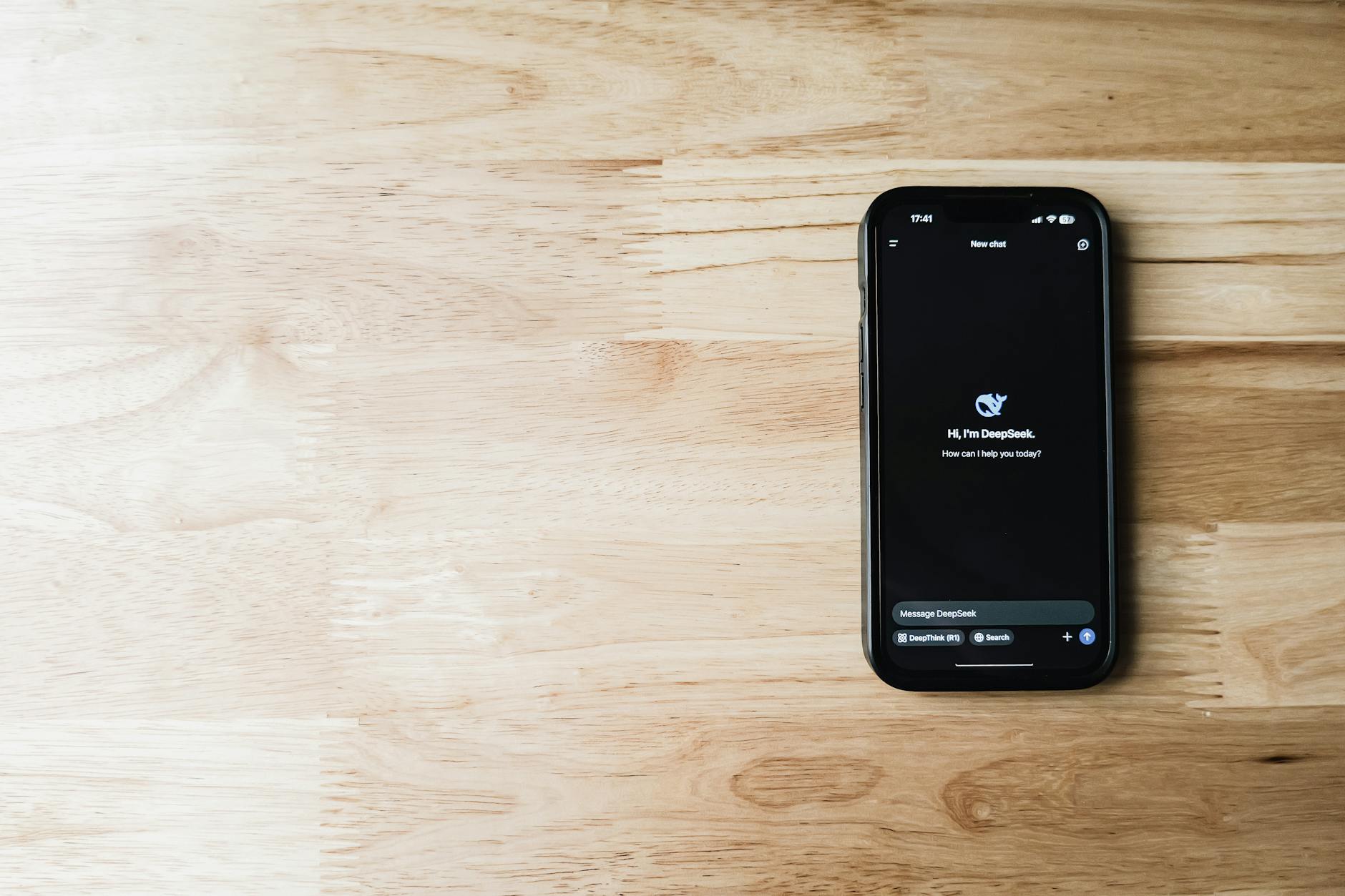 A smartphone featuring an AI assistant app, placed on a light wooden table, showing tech and communication.