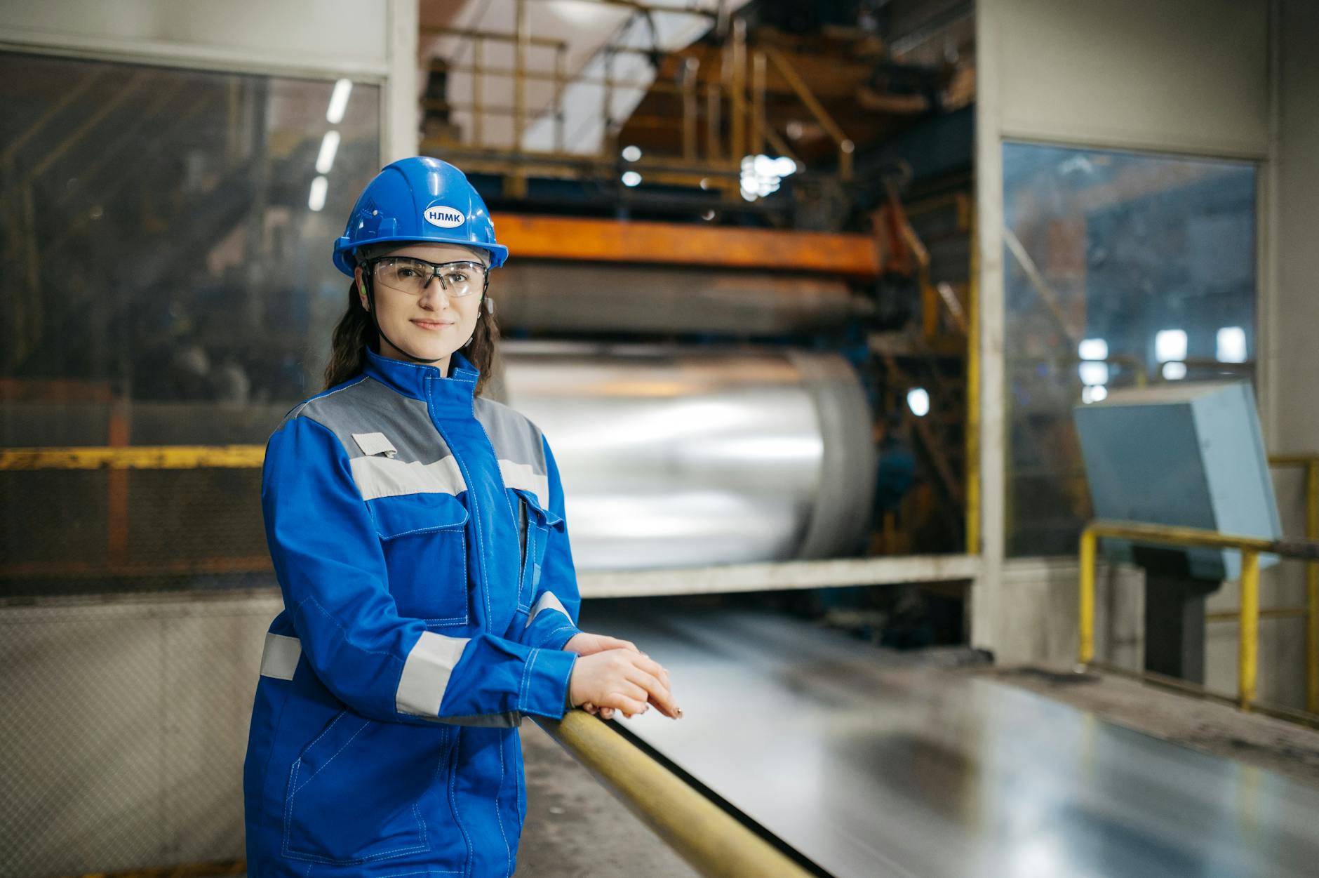 Female factory worker in blue uniform and safety gear inside an industrial facility.