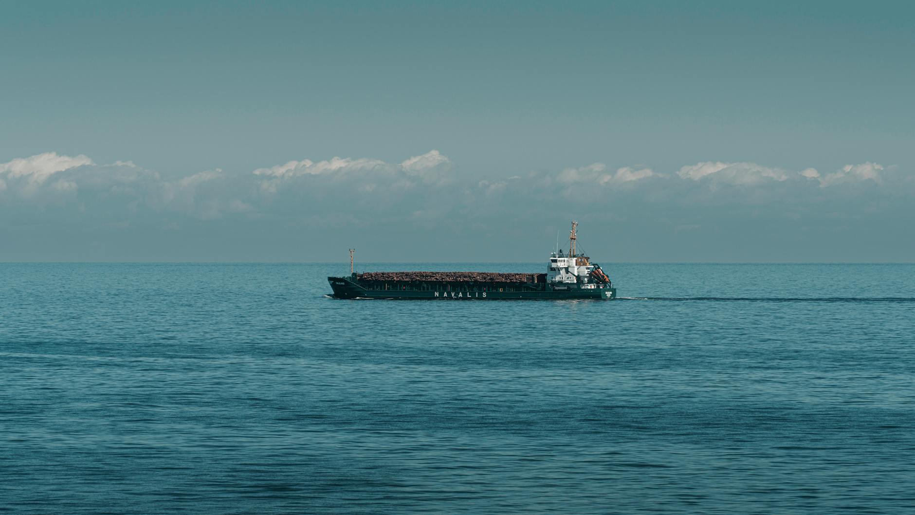 A cargo ship cruising through calm ocean waters under a clear sky.