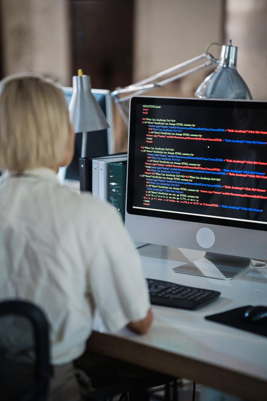 Professional woman coding at office desk with two monitors and desk lamps.