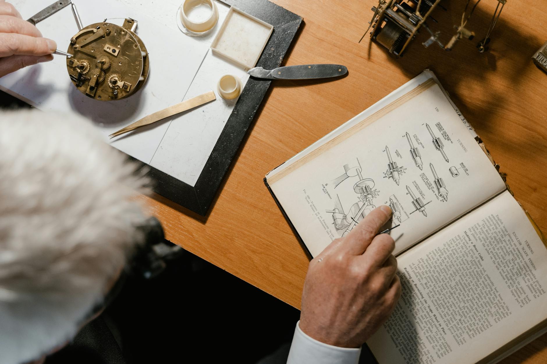 Senior watchmaker referencing manual while fixing a clock mechanism at his desk.