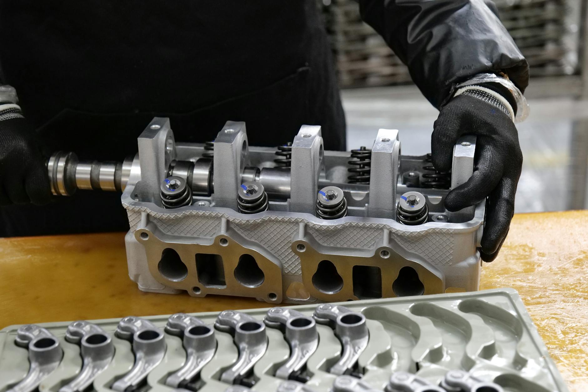 Mechanic assembling an engine cylinder head with precision components on a workbench.