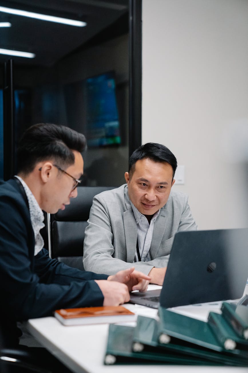 Two men engaged in a business discussion over a laptop in a contemporary office.