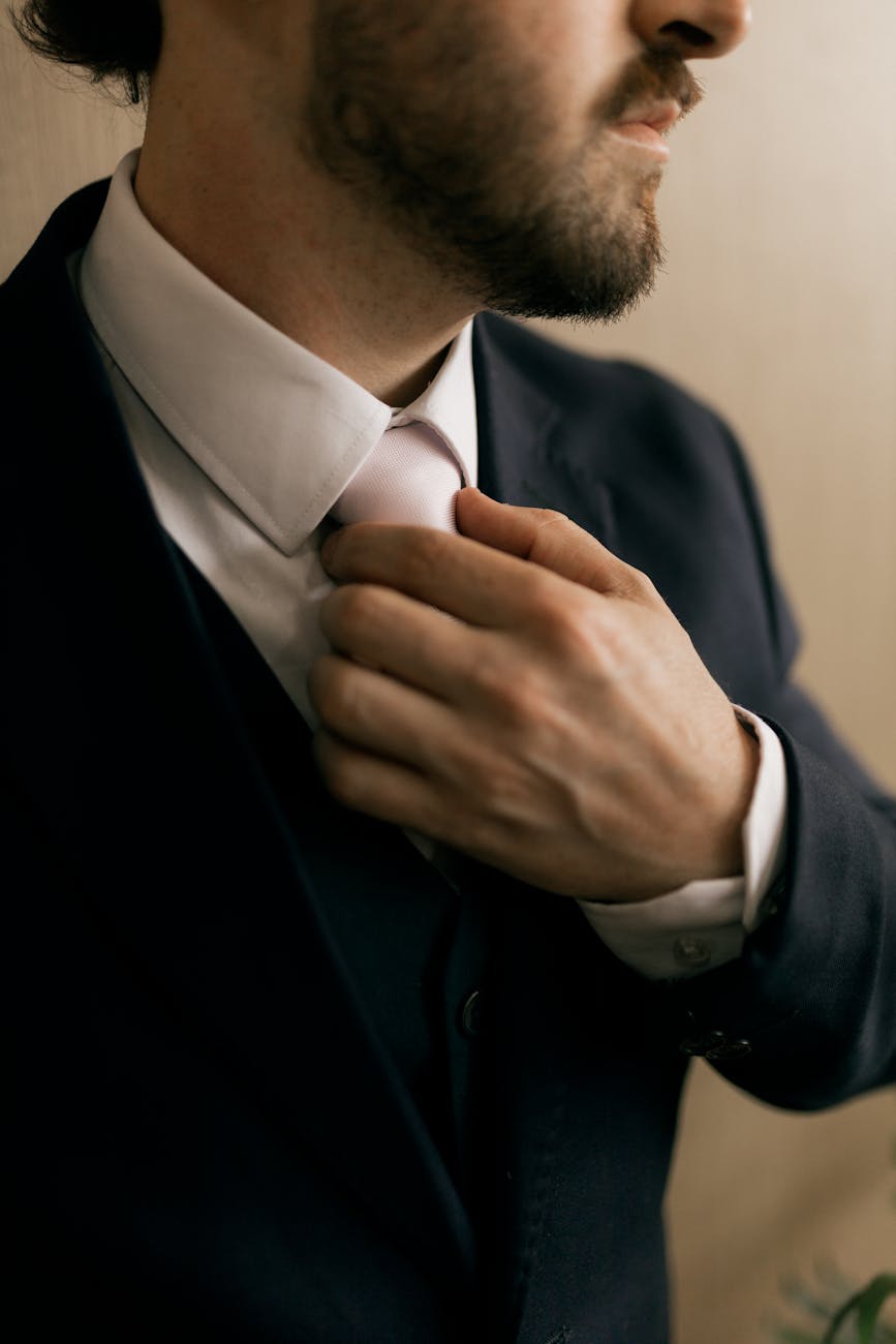 Close-up of a man in formal business attire adjusting his tie, highlighting professionalism.