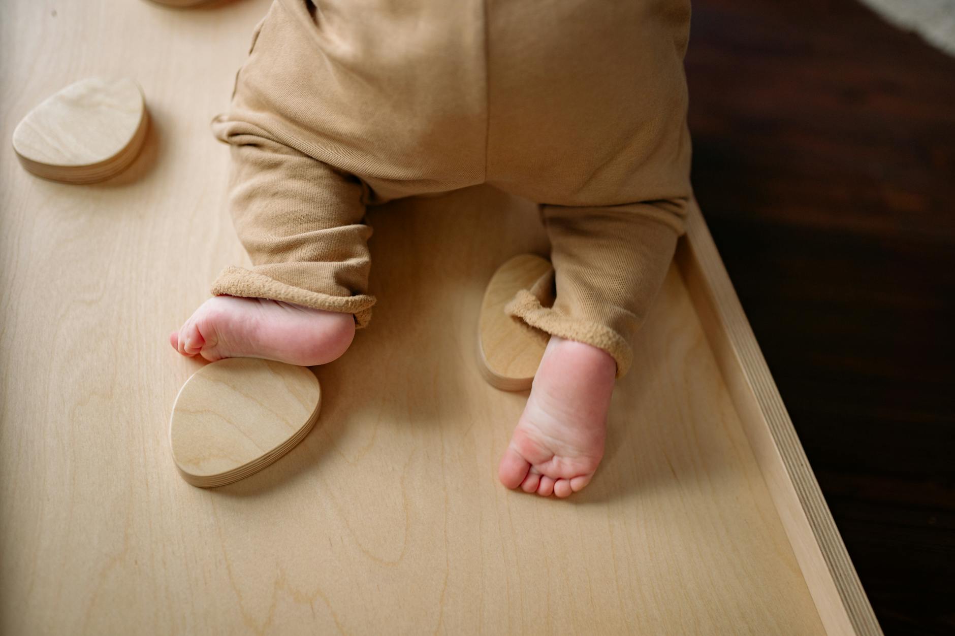 Close-up of a baby wearing an onesie climbing on indoor wooden play equipment.