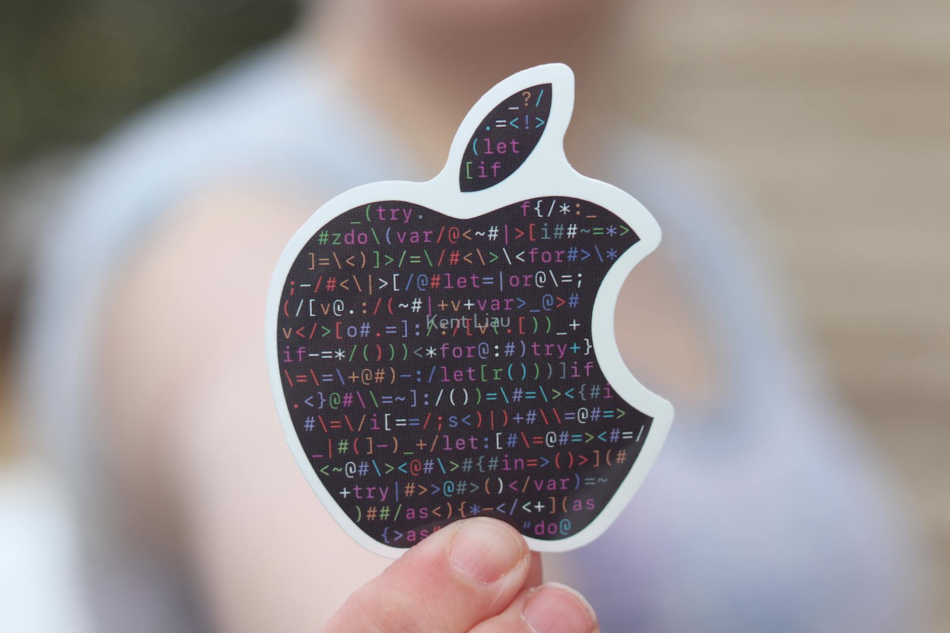 Close-up of a person holding an apple-shaped sticker with binary code, symbolizing technology.